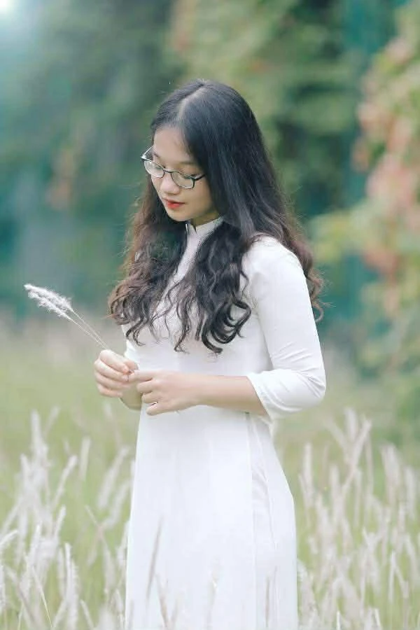 Con gái mặc áo dài trắng đứng giữa cánh đồng cỏ lau
